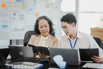 Asian office worker discussing with younger colleagues over laptops in a meeting room, possibly...