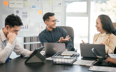 diverse group of Asian professionals, including middle-aged and mature individuals, gathered around a table in a business setting, discussing documents with focused attention.