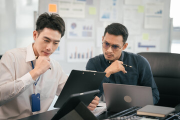 Obraz premium diverse group of Asian professionals, including middle-aged and mature individuals, gathered around a table in a business setting, discussing documents with focused attention.