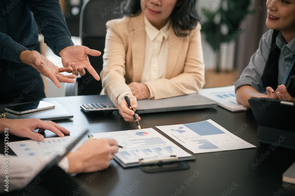 Wall mural diverse group of Asian professionals, including middle-aged and mature individuals, gathered around a table in a business setting, discussing documents with focused attention.