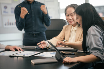 diverse group of Asian professionals, including middle-aged and mature individuals, gathered around a table in a business setting, discussing documents with focused attention.