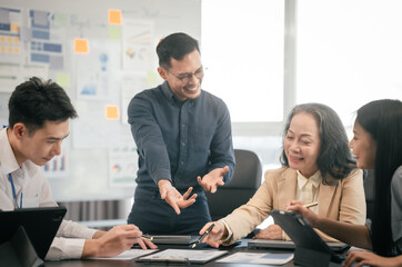 diverse group of Asian professionals, including middle-aged and mature individuals, gathered around a table in a business setting, discussing documents with focused attention.