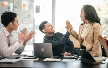 diverse group of Asian professionals, including middle-aged and mature individuals, gathered around a table in a business setting, discussing documents with focused attention.