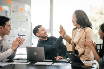 diverse group of Asian professionals, including middle-aged and mature individuals, gathered around a table in a business setting, discussing documents with focused attention.
