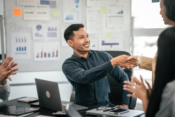 diverse group of Asian professionals, including middle-aged and mature individuals, gathered around a table in a business setting, discussing documents with focused attention.
