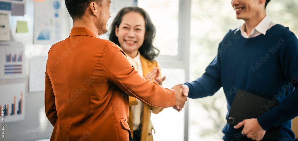 Wall mural Asian middle-age man and mature woman professionals engaged in boardroom meeting. presents data from clipboard to his colleagues, suggesting annual review or planning session.