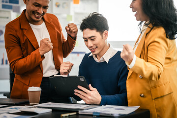 Asian colleagues are in a bright office, celebrating a moment of success. They are gathered around a tablet, with expressions of joy and achievement.