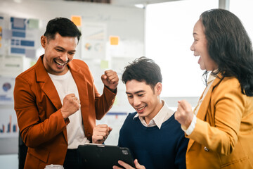 Asian colleagues are in a bright office, celebrating a moment of success. They are gathered around a tablet, with expressions of joy and achievement.