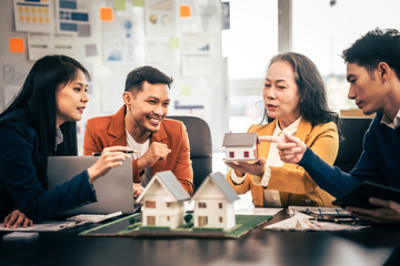 Asian real estate team engaged in a discussion, with two men and a woman focusing on a house model on a table, suggesting a planning or sales meeting.