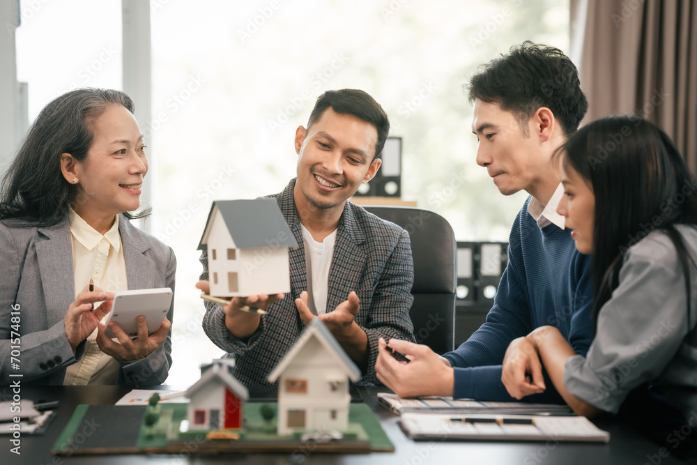 Wall mural asian real estate team engaged in a discussion, with two men and a woman focusing on a house model o