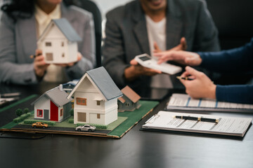 Asian real estate team engaged in a discussion, with two men and a woman focusing on a house model...