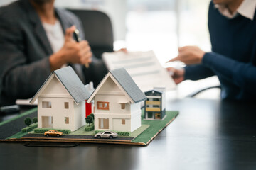 Asian real estate team engaged in a discussion, with two men and a woman focusing on a house model on a table, suggesting a planning or sales meeting.