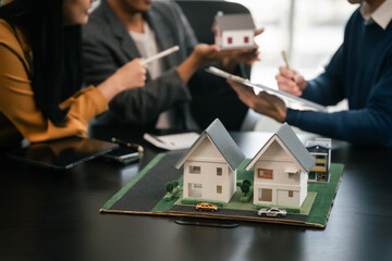 Asian real estate agent team engaged in a discussion, with two men and a woman focusing on a house model on a table, suggesting a planning or sales meeting. - obrazy, fototapety, plakaty