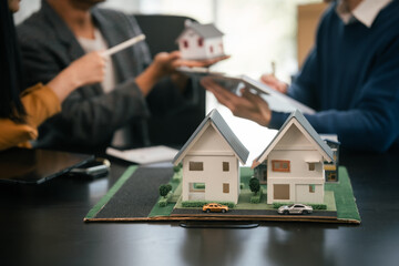 Asian real estate agent team engaged in a discussion, with two men and a woman focusing on a house model on a table, suggesting a planning or sales meeting.