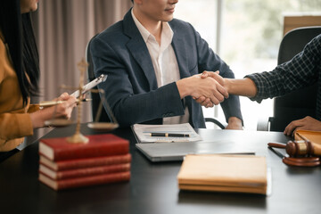 Asian woman yellow top shaking hands with someone across table, while Asian man in suit observes. Legal scales and books visible. legal, legislation