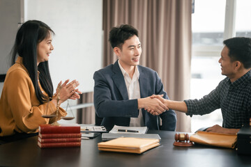 Asian woman yellow top shaking hands with someone across table, while Asian man in suit observes....