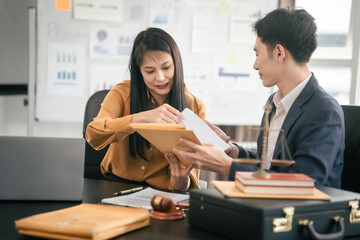 Asian man and woman collaborating professional setting, law office. reviewing documents on tablet, with laptop, contract papers, law books, and justice scale on the desk.