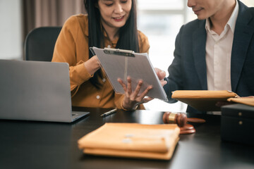 Asian man and woman collaborating professional setting, law office. reviewing documents on tablet, with laptop, contract papers, law books, and justice scale on the desk.