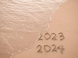 Handwritten inscription 2023 and 2024 on the beach in the sunset time. The concept of Goodbye 2023 and Happy New Year 2024