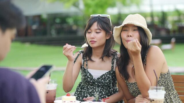 Happy young Asian man and woman enjoy outdoor lifestyle travel nature and cafe on summer holiday vacation. Generation z people friends eating cake and drinking coffee together at outdoor restaurant.
