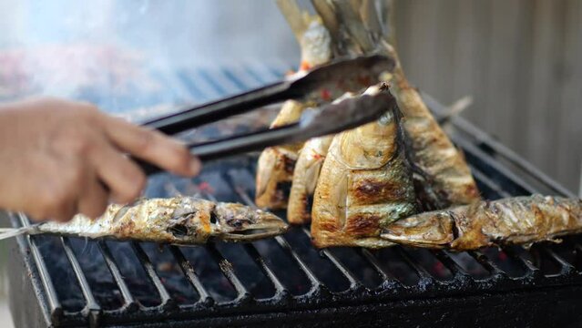Close-up shot of cooking fish. Baking and roasting marinated fish on barbecue grill. Sea bass or grouper grilled over charcoal. 4K	