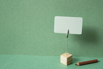 Memo pad with holder and colored pencil on desk. green wall background. copy space