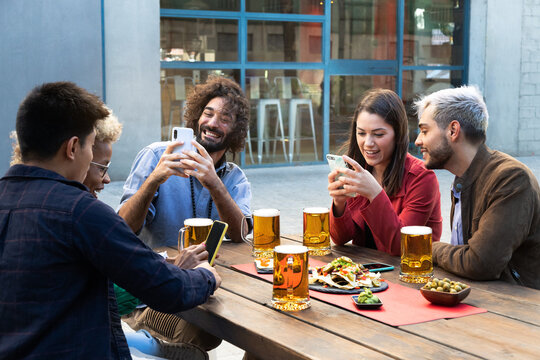 Group of multiracial friends using mobile phones, taking photos and using social media in a bar.