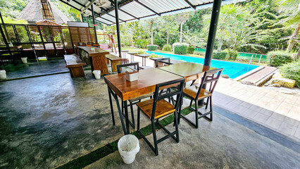 Early morning in outside traditional restaurant wooden Chairs, wooden table beside the pool and garden view. Empty outdoor restaurant garden. The wood table on natural restaurant empty covered patio.