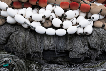 A pile of commercial fishing nets on a quay, white and red plastic floats and nets and ropes. - obrazy, fototapety, plakaty