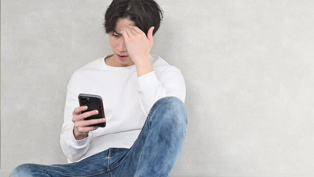 壁に寄りかかり困る表情やネガティブな表情や笑顔になるスマホを持つハンサムな男性の動画