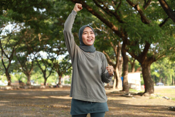Running, portrait and an asian muslim woman celebrate outdoor for exercise, training or fitness goals with a fist in nature for a workout, run and performance target, success or win