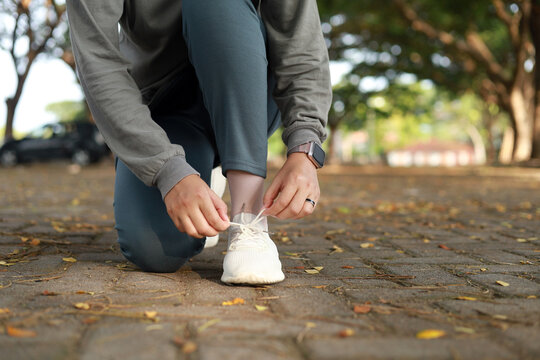 Close up photo of A Muslim woman in her sports clothes squats and fixes her shoelaces while exercising in the park