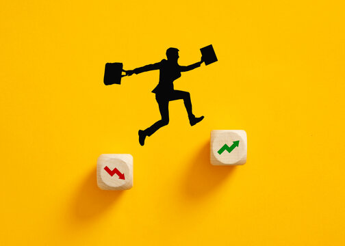 Silhouette of a businessman jumping from decline symbol to growth symbol on wooden cubes.
