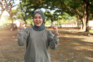 Portrait fit asian muslim female fitness runner joyful and excited after running. Woman pumping fists. Success in sport training wellness concept. Positive face expression emotion