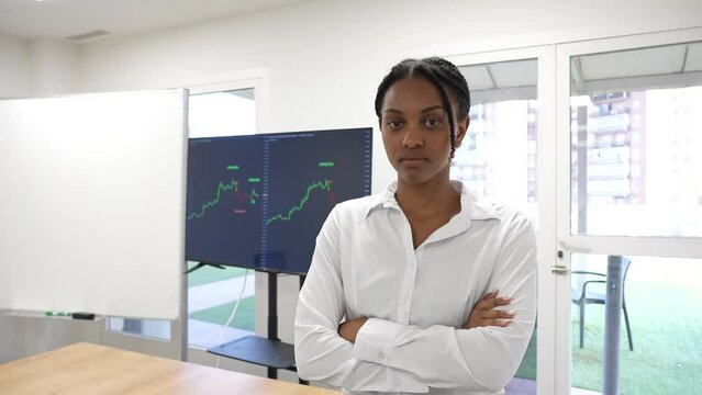 Black African business woman looking at camera with a trading view graphic in the background serious face expression. Success money trader stock market woman empowerment.
