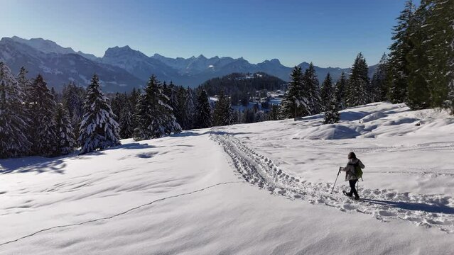 Aerial tracking shot of person with ski poles hiking on snowy mountain during sunny day in Swiss alps - beautiful landscape in winter