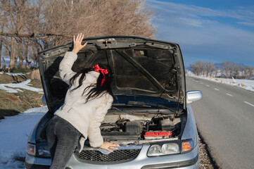 back of girl with a sexy ass looks under hood at the engine of a broken car on road in winter