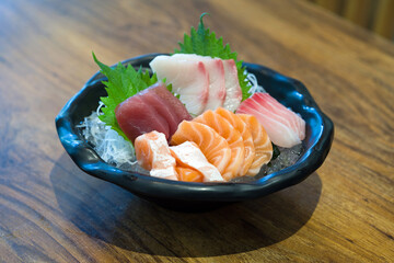 A tantalizing display of Japanese sashimi, elegantly served in a pristine bowl, resting on a rustic wooden table. Experience the vibrant colors and delicate freshness of this traditional delicacy.