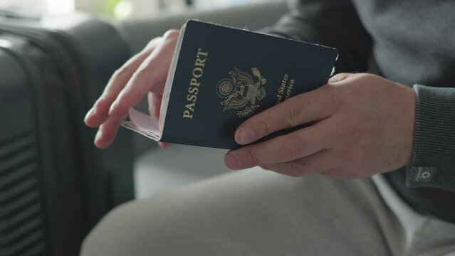 Close up of Man's hand, holding a US passport. Luggage in background.