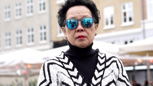 asian senior woman wearing sunglasses walking in Europe downtown