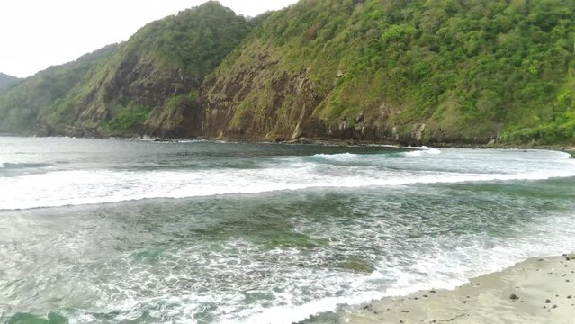Drone shot on Papuma Beach, Jember, Indonesia with thick vegetations, towering cliff and ocean waves.