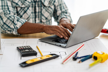 Close up Asian individual architect or engineer holding building scale model of multi-story building. design or review of architectural plans laid out on work surface in front of them.