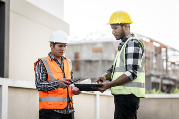 Asian people, two man, holding blueprints Structural engineers examine structural plans for office buildings and housing developments on-site, discussing work at construction site.