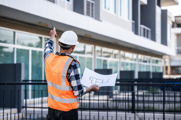 engineer in a high-visibility vest and hard hat, intently reviewing a document or blueprint, with a modern building in the background.