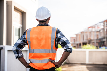 engineer in a high-visibility vest and hard hat, intently reviewing a document or blueprint, with a modern building in the background.