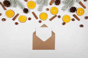 Christmas composition, dried orange slices, fir tree branches, cinnamon sticks, pine cones, hazelnuts on white background. Kraft envelope, white card. Top view, flat lay, copy space.