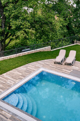 Two sun loungers stand next to a rectangular pool in the garden. Top view
