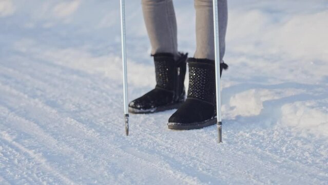 female legs in ugg boots with Scandinavian walking poles on snow-white clean snow