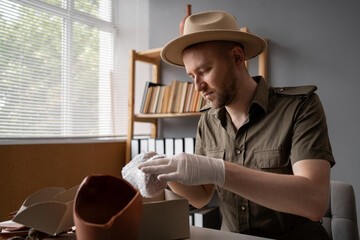 Archaeologist or digger in a hat working in an office, packing antique dishes for sale