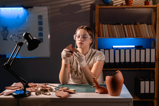 Female archaeologist studying an ancient vase working late at night in her office